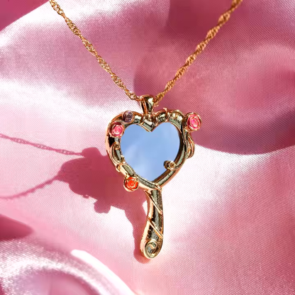 Mirror of Venus Necklace hanging on a pink satin background, featuring a heart-shaped mirror and floral accents.